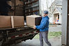 An EZ MoveIt professional mover in a blue uniform carefully loading moving boxes into a truck for a long-distance relocation service.