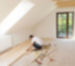 Handyman installing hardwood flooring in attic room — part of floor repair and replacement services