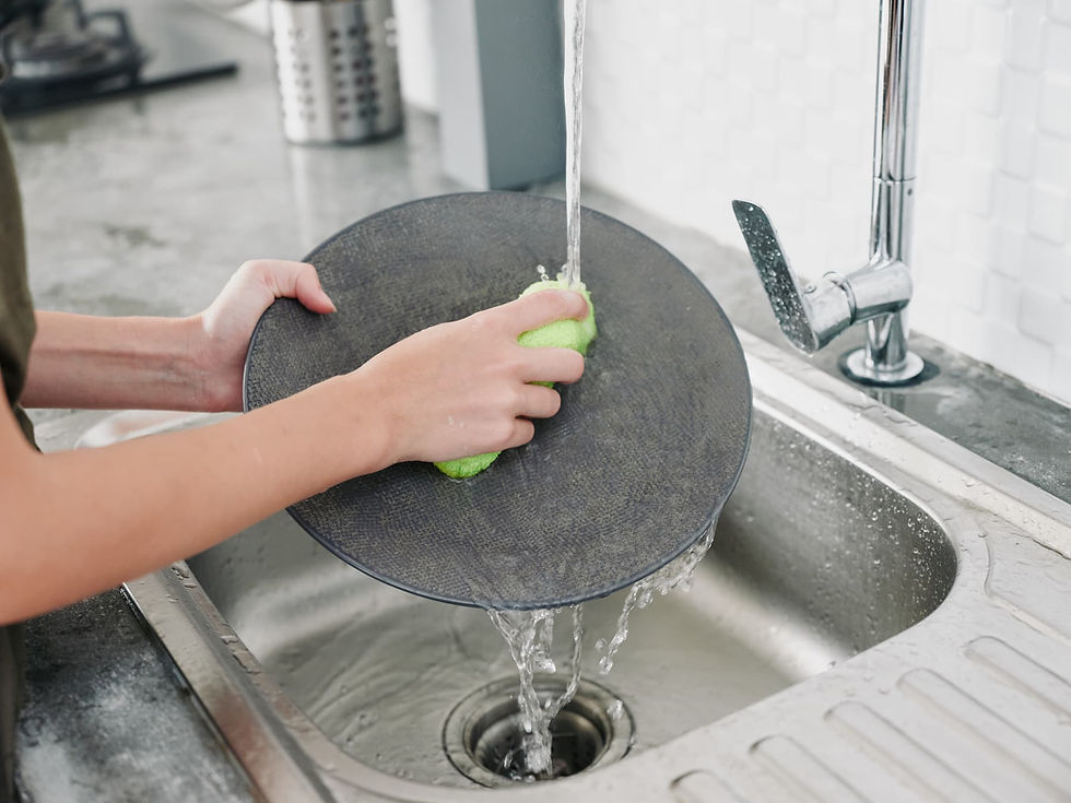 Person washing dishes in a kitchen sink with slow drainage, highlighting the need to prevent clogged drains.