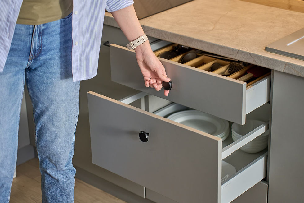A person opening a grey kitchen drawer, showcasing organized cutlery and plates as part of modern cabinet storage systems.