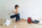 A frustrated homeowner sitting barefoot on a step ladder in front of a half-painted wall, surrounded by painting tools — illustrating the challenges of DIY painting without proper wall preparation.