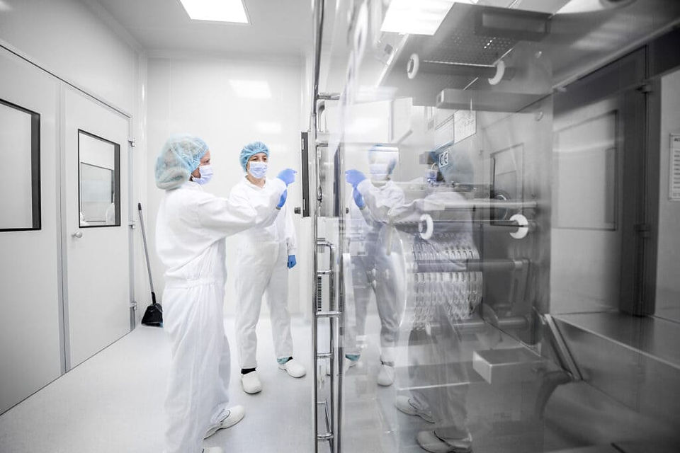 Profissionais em trajes de proteção trabalhando em laboratório limpo com equipamentos industriais.