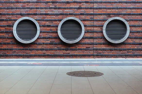 Three circular grills along a brick wall echo the round manhole cover on the ground.