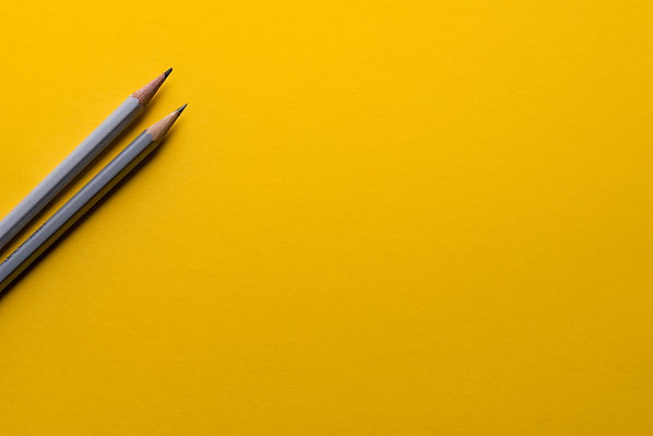 The image shows two gray pencils stretched out on a mustard-yellow backdrop.