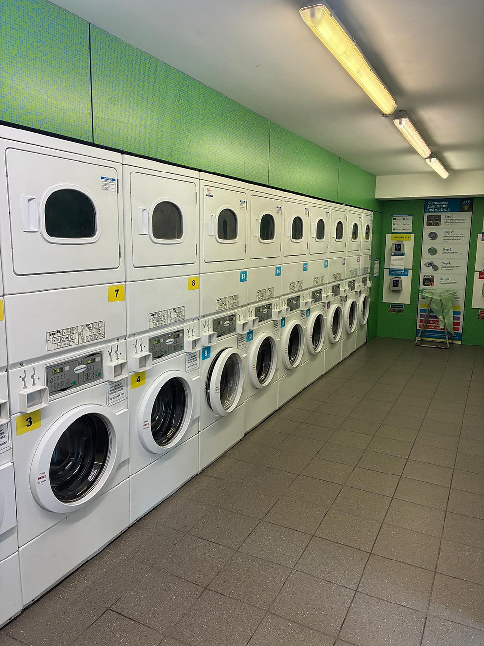 Old laundry, Row of white washing machines and dryers in a laundromat with green walls. Bright lighting and instruction signs visible. 