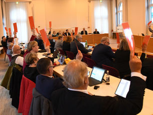 Zahlreiche Menschen bei einer Sitzung halten Karten zur Abstimmung hoch.