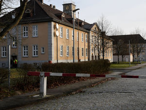 Kasernengebäude hinter einer Schranke an einer Straße aus Pflastersteinen.