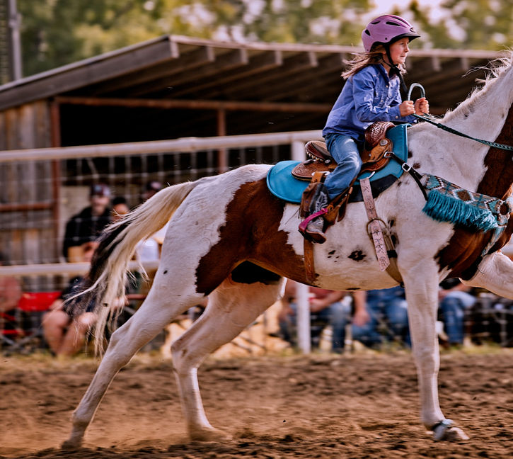 Young girl riding a horse in a speed race with a crowd watching.