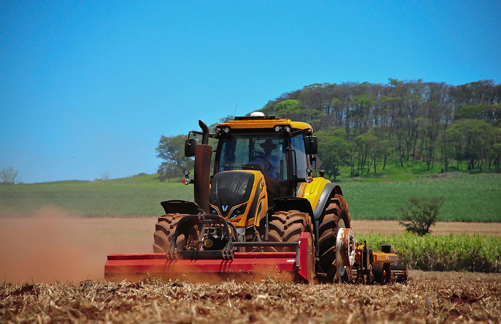 Yellow tractor tilling a field with dust rising.