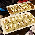 Two trays of pierogi topped with sour cream.