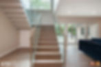 Small wooden staircase with glass railing and view to the backyard.