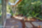 Walkway to the backyard surrounded by lush green trees and bushes.