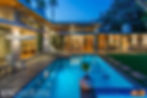 Backyard view of contemporary home with tall glass walls and a pool.