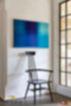 Small vintage wooden chair under modern blue art piece contrasted by the natural light.