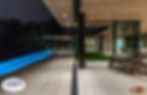 Modern home with open top to bottom glass windows, overlooking ground level pool at night.