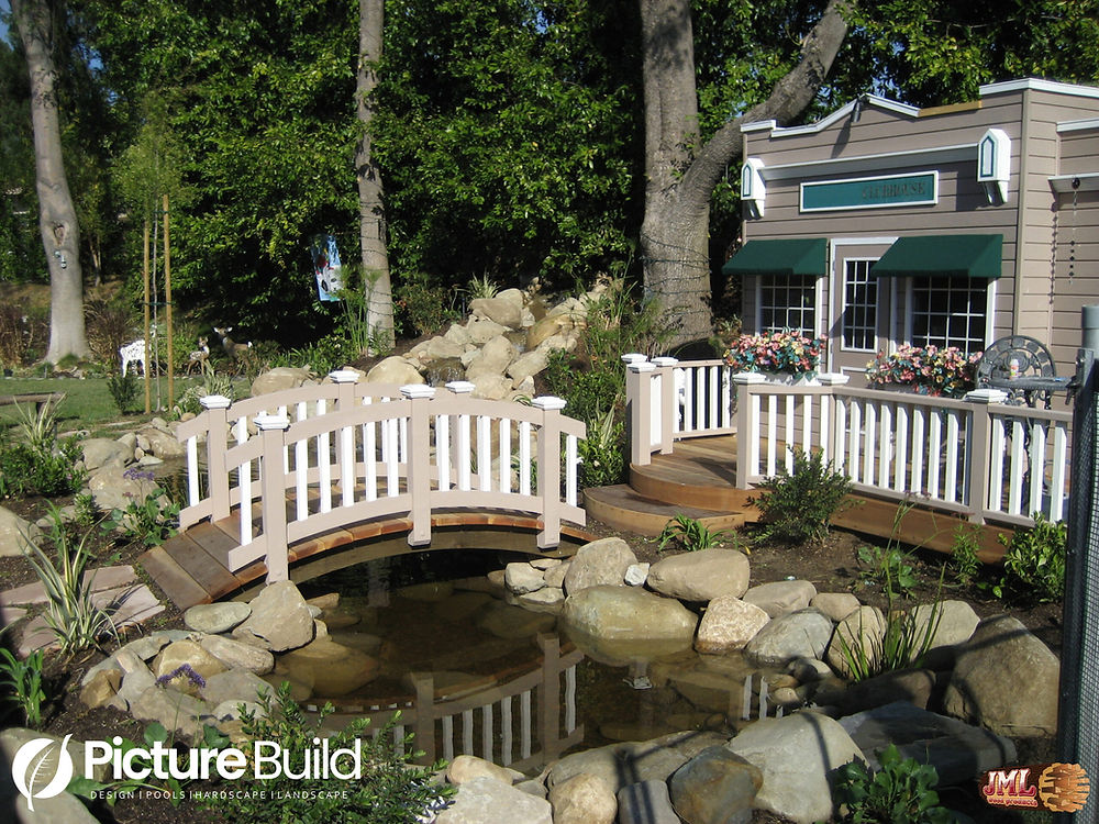 Backyard view of pond and custom bridge leading to custom playhouse