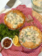 Two Over-The-Top Zuppa Toscana Pot Pies are arranged on a red checkered cloth with a bunch of parsley to the left side and 2 golden forks on the right side.