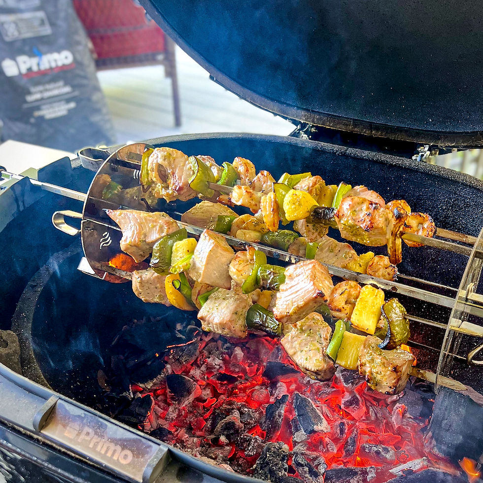 A rotisserie on a Primo Grill with skewers of fish, peaches, and peppers.