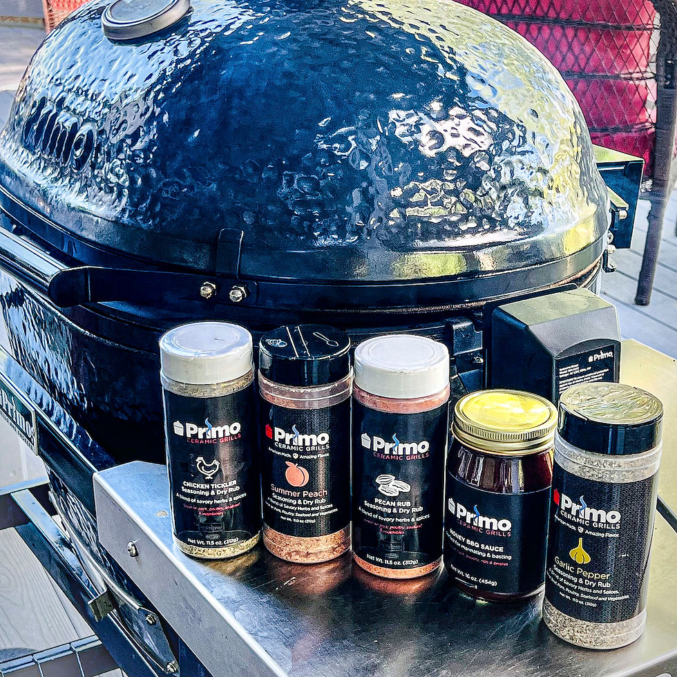 Four different Primo Grill rubs and 1 Primo Grills BBQ sauce are positioned in from of a Primo Ceramic XL OVAL 400 Grill.