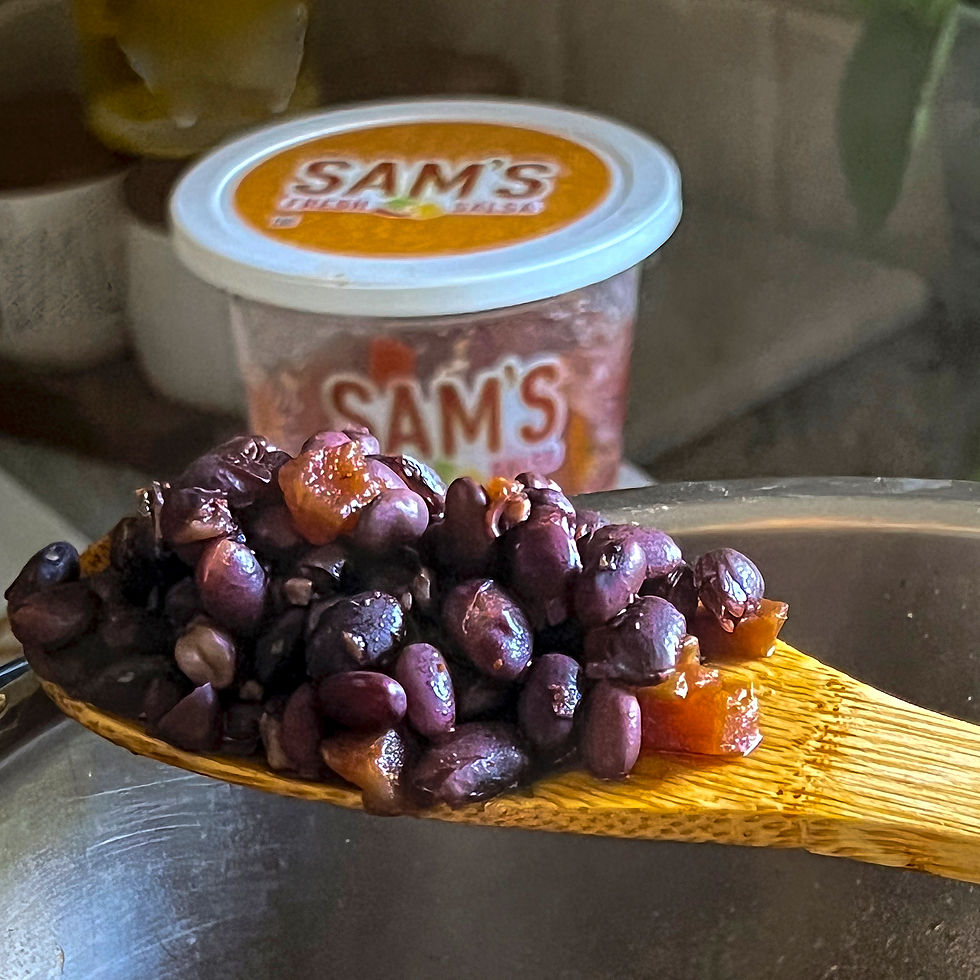 A wood spoon holds black beans with bits of tomato from Sam's Fresh Salsa.