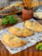 3 Calzone are on a serving board with parsley and salad in the backdrop.