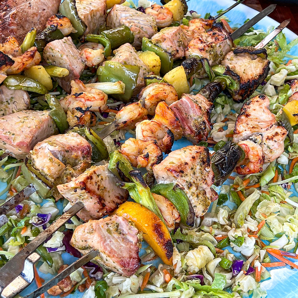 A close up platter of fish, peaches, peppers, and shrimp that have been cooked on the grill using the Primo Rotisserie Kebab Holder.