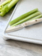 A paring knife is used to cut a celery stick into 3 long slices before chopping.
