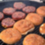 Burgers are on the grill with sesame seed buns toasting.