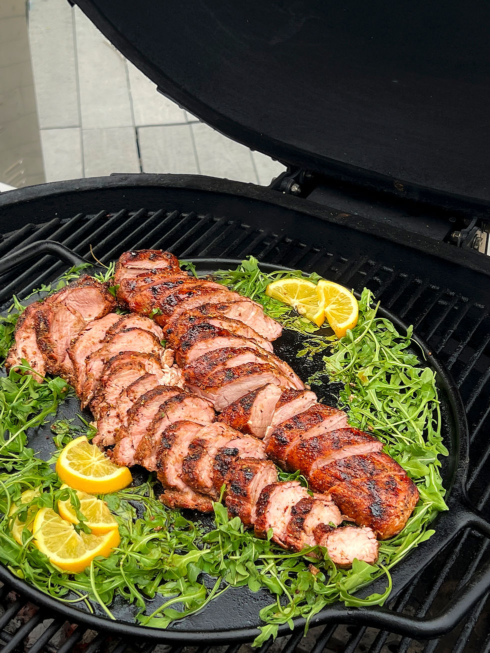 A cast iron pan is on a grill with arugula and sliced pork tenderloin.