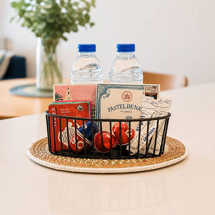 Welcome basket in a modern apartment in Porto with bottled water, coffee capsules, tea, sugar, and a local chocolate, ready for arriving guests.