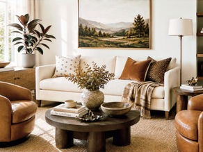 Earthy sitting room with an ivory sofa, caramel leather chairs, dark wood coffee table, camel throw, warm brown pillows, brass floor lamp, landscape artwork, natural woven rug, and potted rubber tree.