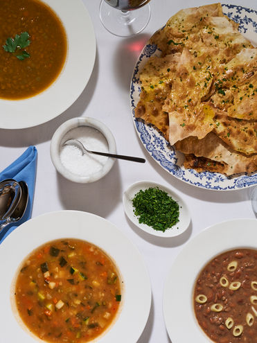 Three bowls of Italian soups with fresh herbs and crispy housemade flatbread on a white tablecloth at Casa Tevere kosher restaurant in NYC.