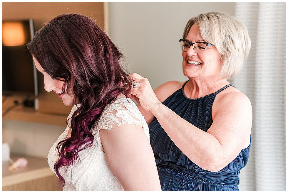 Happy Mother of the bride putting bride's dress on at the hotel
