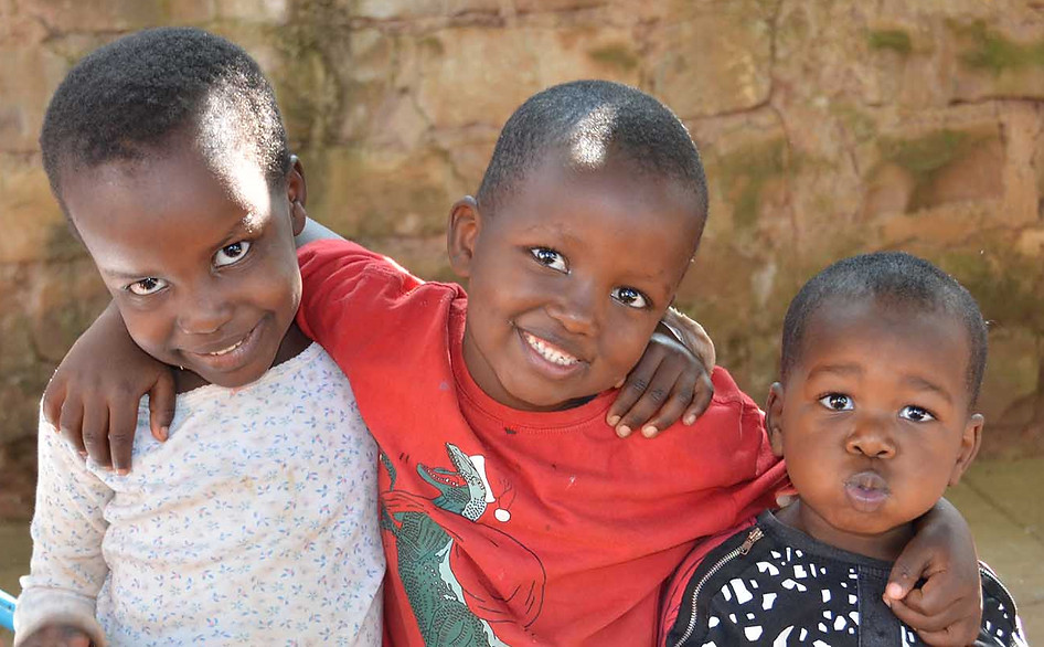 Three young children smiling and hugging together.