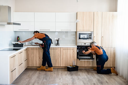 Two handymen, workers in uniform fixing, installing furniture and equipment in the kitchen
