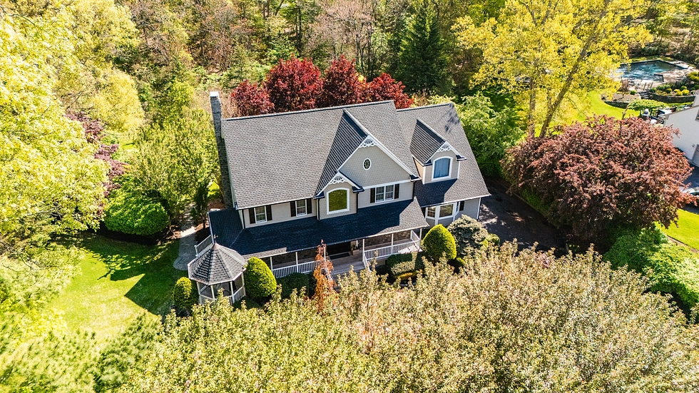 Aerial view of a two-story house, surrounded by a well-kept lawn and trees. Driveway and neighboring homes visible. Sunny day.