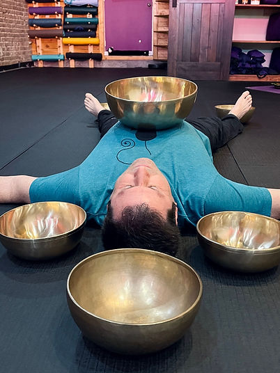 man laying down with metal tibetan bowls on and around him