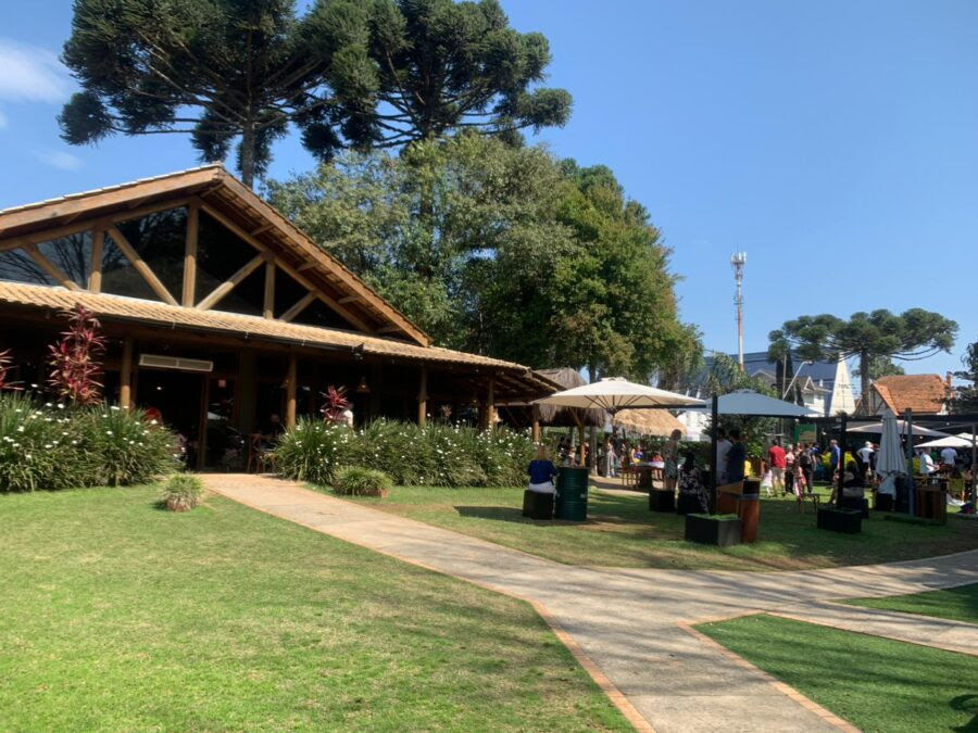 Área externa do Espaço Depósito, em Curitiba, com amplo gramado, restaurante e ambiente aberto para receber visitantes.