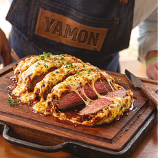 Prato de carne servido no Vila Yamon, com corte bovino coberto por queijo derretido sobre uma tábua de madeira.