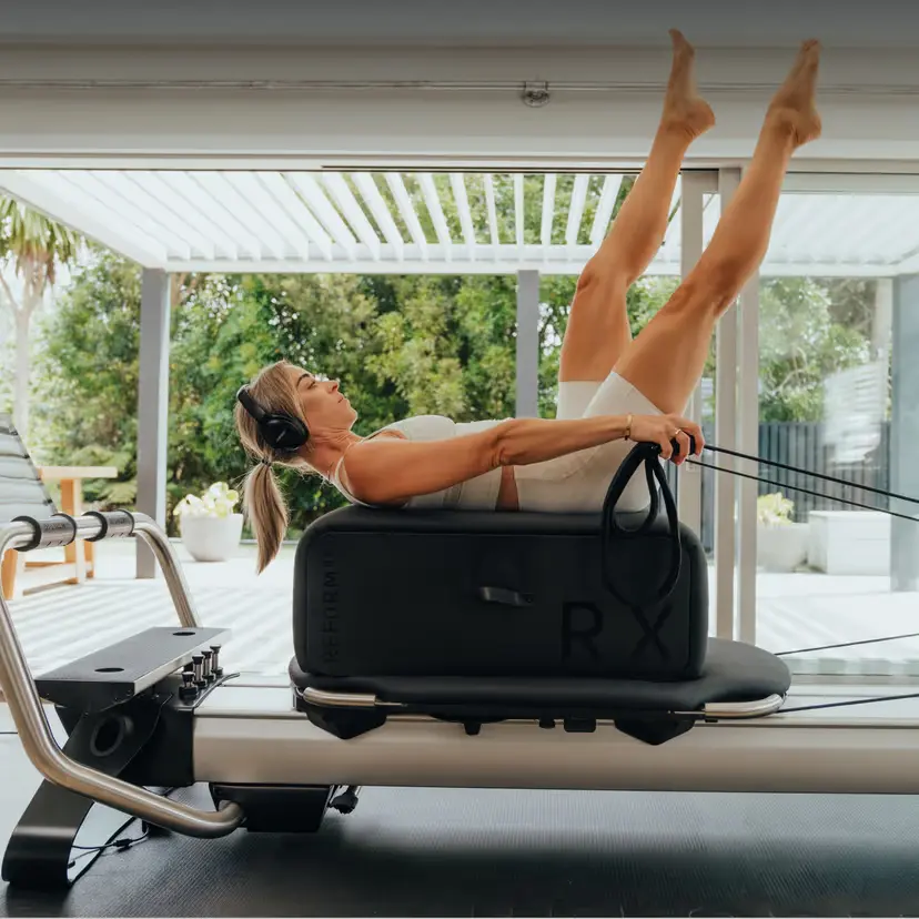 Eine einzelne Frau in beiger Fitnesskleidung trainiert pilates an ihrem NordicTrack Ultra 1 Reformer RX-S in einem hellen Raum