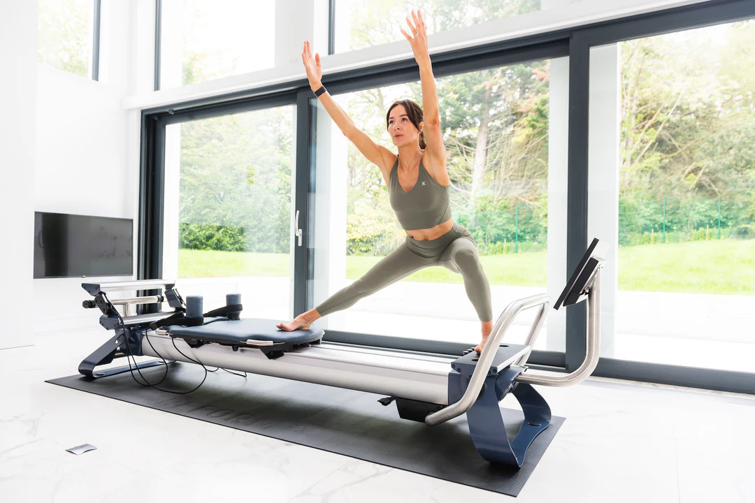 Eine einzelne Frau in grüner Fitnesskleidung trainiert pilates an ihrem NordicTrack Ultra 1 Reformer RX-S in einem hellen Raum