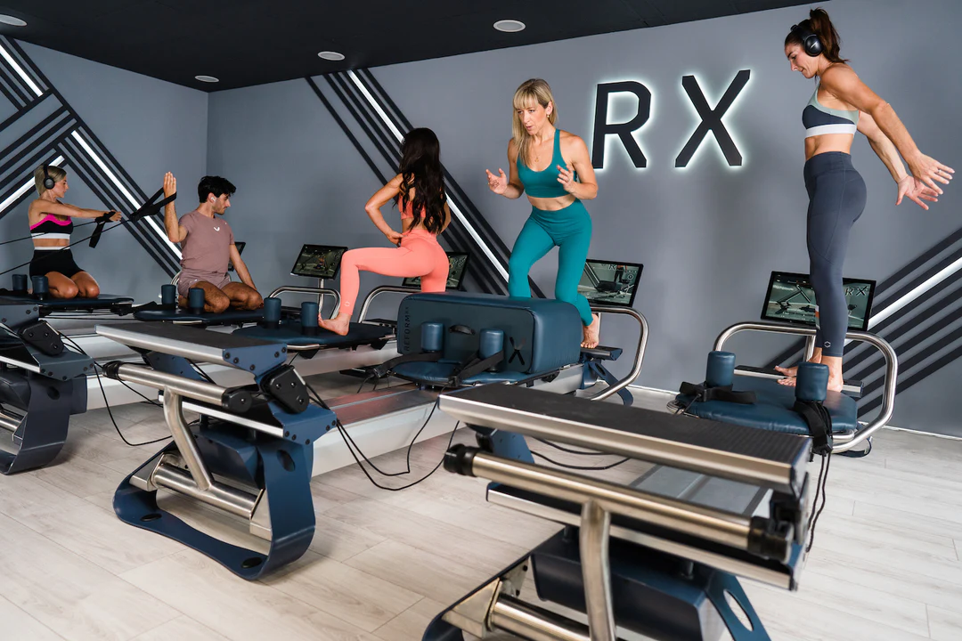 Eine Gruppe von Männern und Frauen trainieren gemeinsam mit einer Lehrerin NordicTrack Ultra 1 Reformer RX-S Geräten in einem modernen Gym