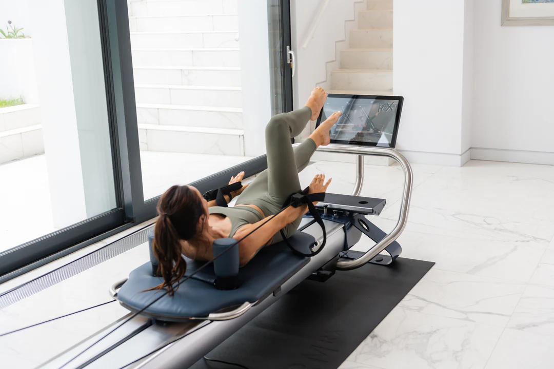 Eine einzelne Frau in grüner Fitnesskleidung trainiert pilates an ihrem NordicTrack Ultra 1 Reformer RX-S in einem hellen Raum