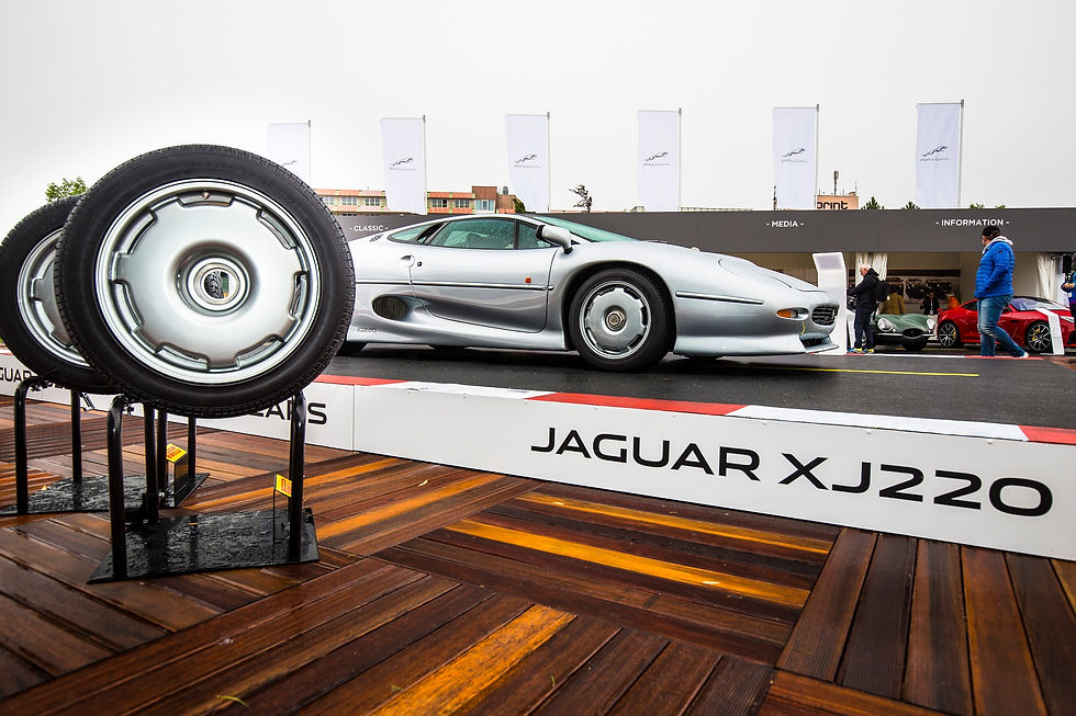 links sind auf Ständern zwei Pirelli-Reifen präsentiert, im Hintergrund steht ein silbernes Jaguar-Modell mit passenden Pirelli-Reifen