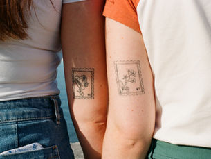 Two people hold hands, facing away, with matching tattoos on the back of their arms.