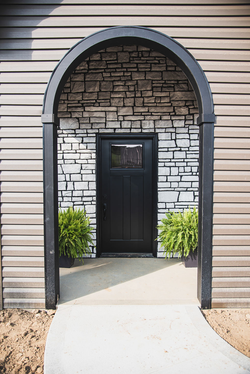Black arched doorway with stone facade and potted ferns.