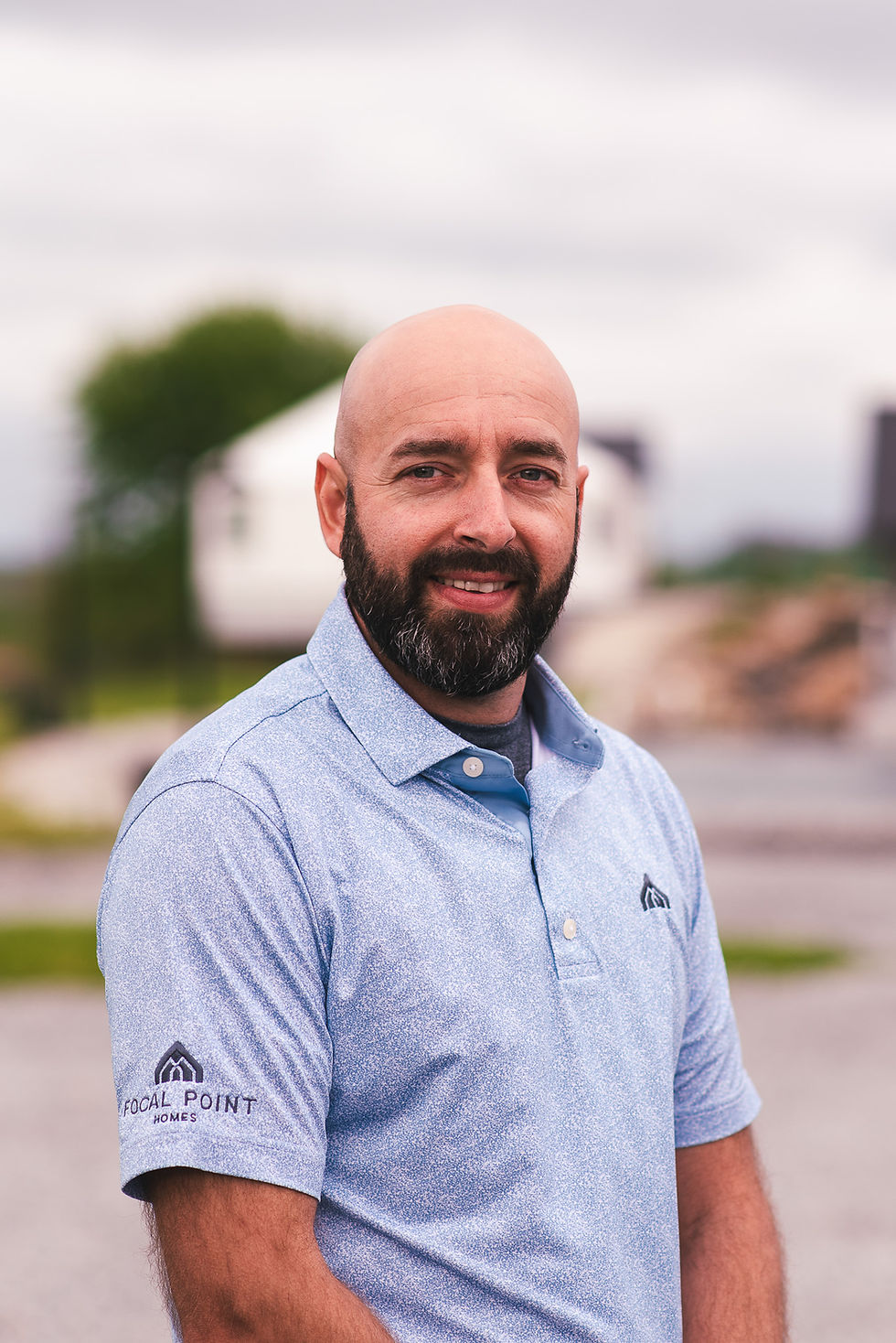 Smiling bald man with a beard wearing a blue polo shirt.