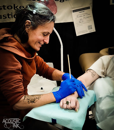 An action shot of Kata handpoking a clients wrist at a tattoo convention.