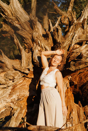 Portraitfotografie München – Frau in hellem Kleid vor Baumwurzel im warmen Licht, fotografiert von Anja Plattner