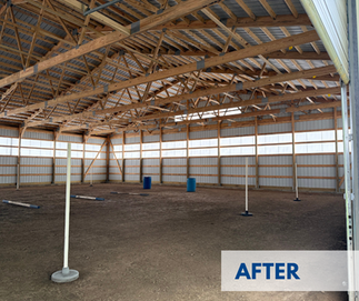 Completed interior of the enclosed riding arena at Giant City Stables, with high wooden trusses, a dirt riding surface, and training equipment in place.